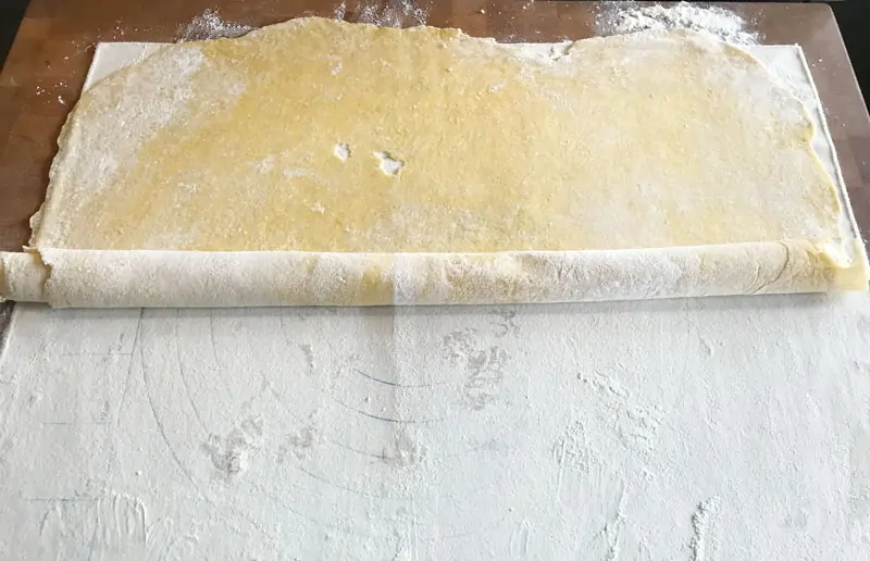 Rolling homemade egg noodle dough into a jelly-roll