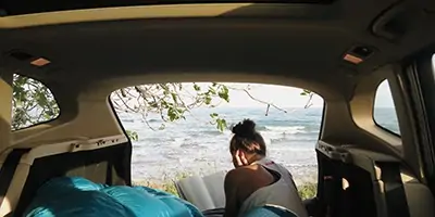 Woman in van reading a book set in California with beautiful landscape in background