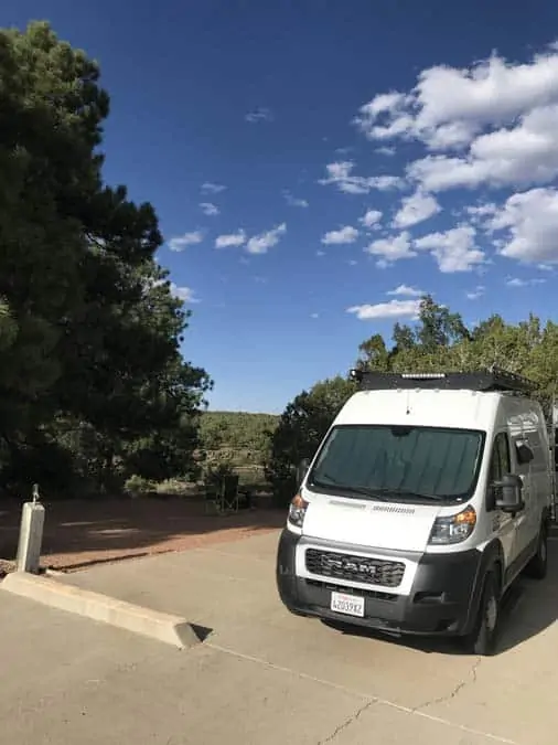 Women camping alone in Fool Hollow Campground.  Show Low, AZ.  Spacious, level campsite pads wit converted Promaster van parked.